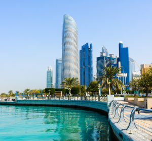 Moderne Skyline von Abu Dhabi mit Hochhäusern an einer Uferpromenade, gesäumt von Palmen und klarem türkisfarbenem Wasser.