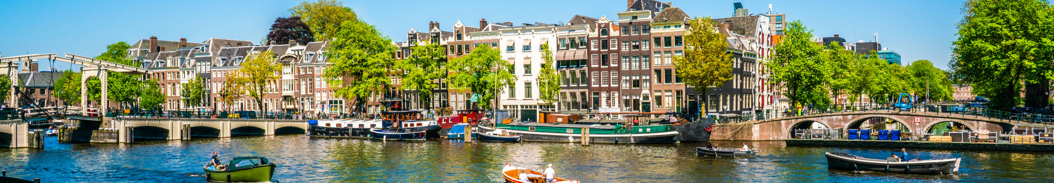 Grachte in Amsterdam mit historischen Häusern, Booten und Brücken bei Sonnenschein