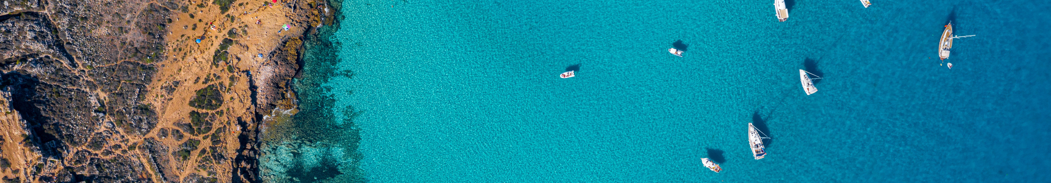 Drohnenaufnahme der Cala Rossa auf Favignana, Ägadische Inseln bei Sizilien, mit türkisblauem Wasser und zahlreichen Booten.