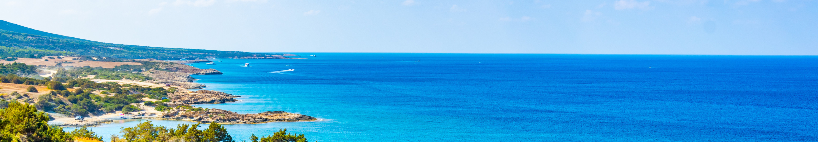 Felsküste mit grün bewachsenen Hügeln und türkisblauem Meer auf Zypern bei klarem Sommerhimmel.
