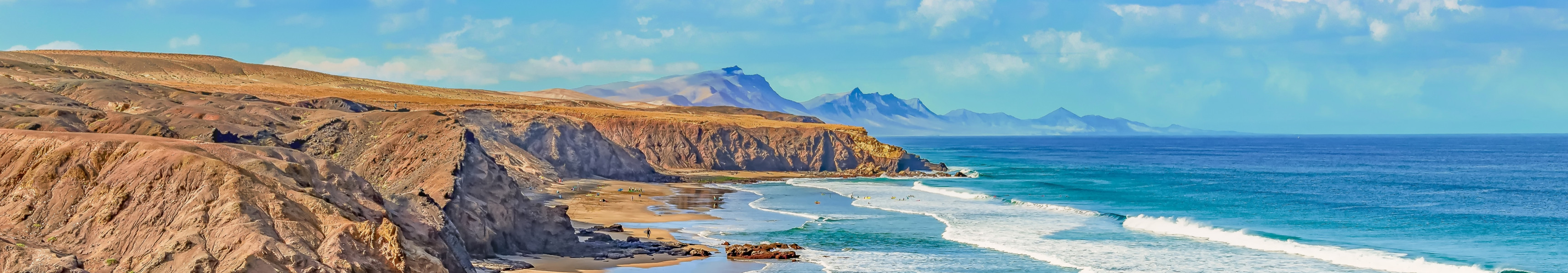 Weitläufiger Sandstrand mit Felsklippen und türkisfarbenem Meer auf Fuerteventura, Kanarische Inseln.
