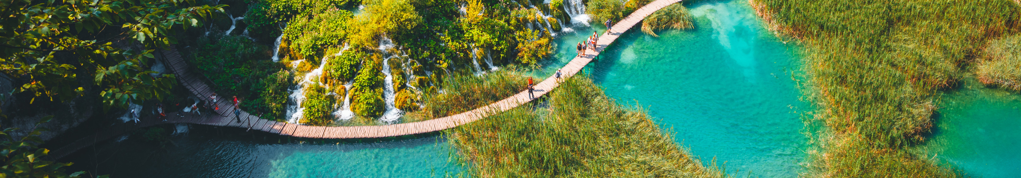 Holzstege führen durch die türkisfarbenen Seen und Wasserfälle des Nationalparks Plitvicer Seen in Kroatien, umgeben von grüner Vegetation und Felsen.