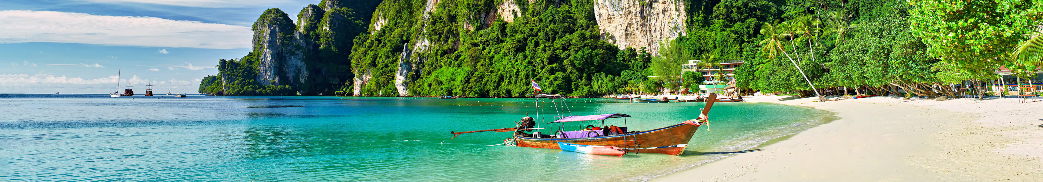 Tropischer Strand mit weißem Sand und türkisfarbenem Wasser, im Vordergrund ein traditionelles Longtailboot
