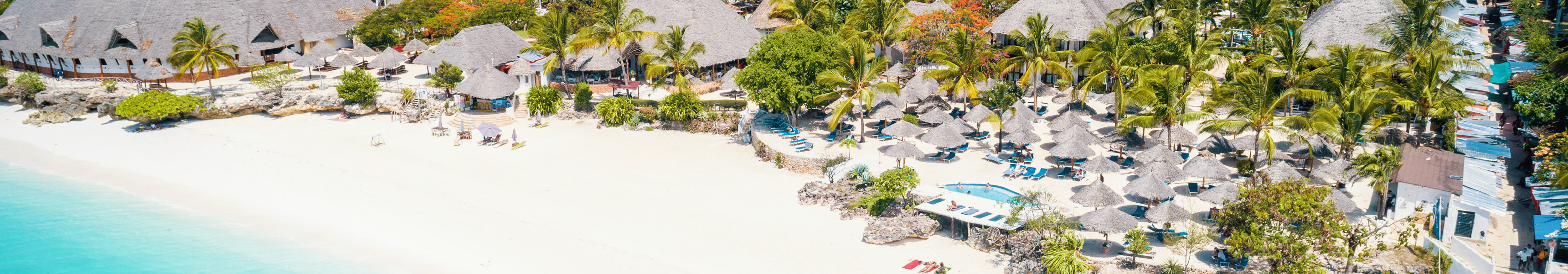 Luftaufnahme von Nungwi Beach auf Sansibar, Tansania, mit weißem Sandstrand, türkisfarbenem Meer, Palmen und traditionellen Strohdachhütten entlang der Küste.