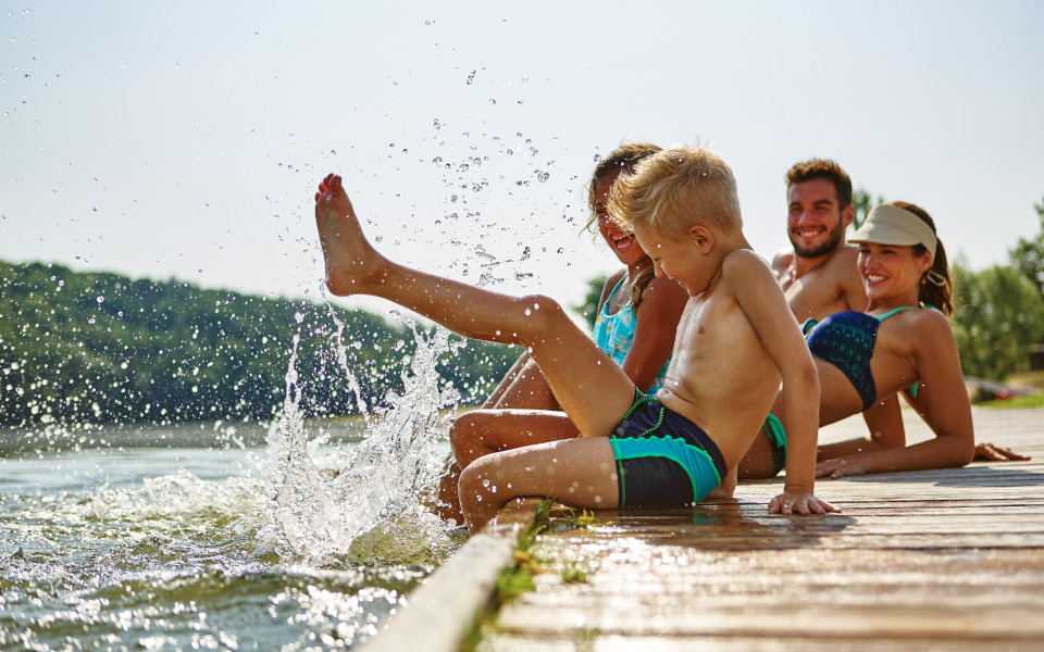 Familie am Gardasee, die am Steg sitzt und mit ihren Füßen im Wasser planscht.