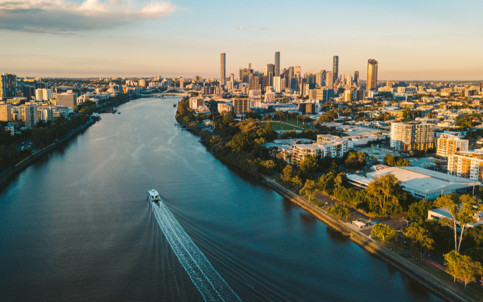 Luftaufnahme von Brisbane bei Sonnenuntergang, w&auml;hrend ein Boot am Brisbane River auf die Stadt zusteuert