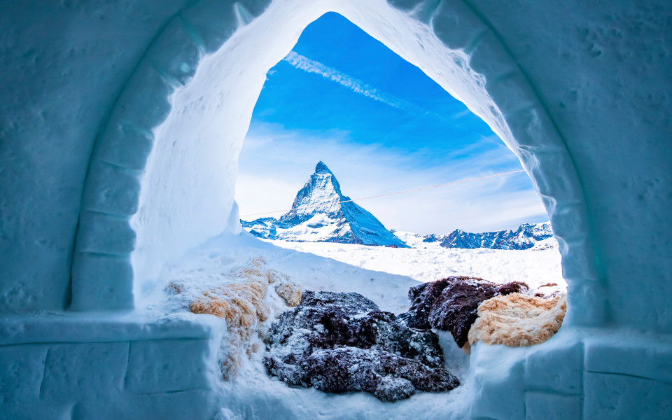 Innenraum eines selbstgebauten Iglus mit malerischem Blick auf die verschneite Landschaft zum Silvesterabend.