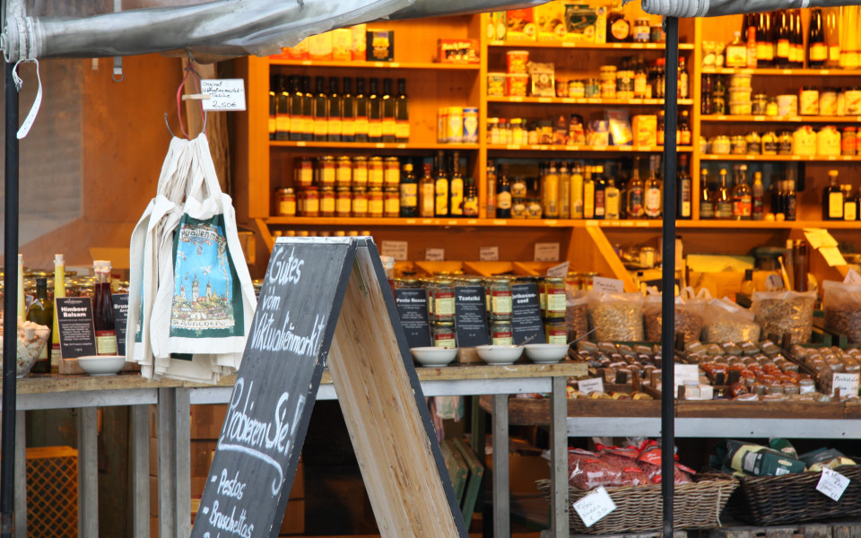 Gem&uuml;tlicher Marktstand auf dem Viktualienmarkt in M&uuml;nchen mit regionalen Spezialit&auml;ten, handgemachten Delikatessen und traditioneller Marktatmosph&auml;re.