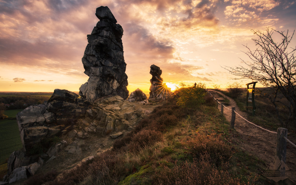 Das Naturwunder Teufelsmauer im Harz, bei Sonnenuntergang, mit markanten Felsformationen und einem Wanderweg im Vordergrund.