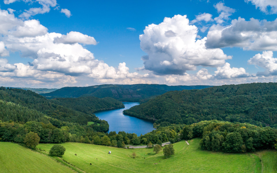 Das Naturwunder Nationalpark Eifel, mit &uuml;ppigen W&auml;ldern und einem malerischen Stausee, eingebettet in sanfte H&uuml;gel und unter einem weiten blauen Himmel.